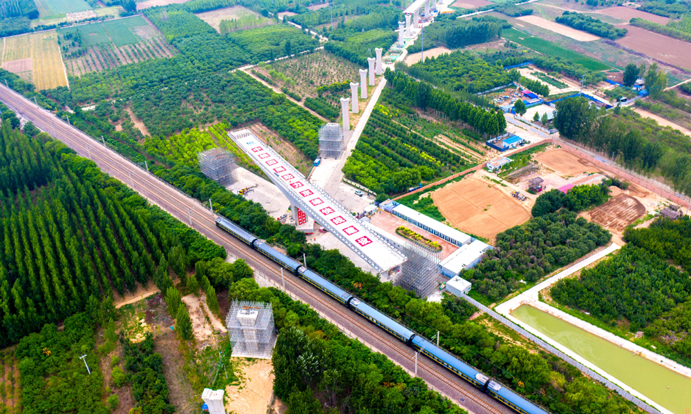 跨京九铁路连续梁是雄安机场快线首座涉及运营铁路的转体梁，所跨京九铁路每日运行列车多达百余列。为确保转体期间京九铁路安全运营，中铁四局多次组织专家评审、优化施工方案，并在正式转体前试转，通过称重平衡试验测试转体部分的不平衡力矩、偏心矩、摩阻力矩及摩擦系数等参数，以实现桥梁转体的配重要求，在转体过程中，根据转台上标识的转角刻度及梁面轴线实行严格监控。图为跨京九铁路转体梁转体前航拍。