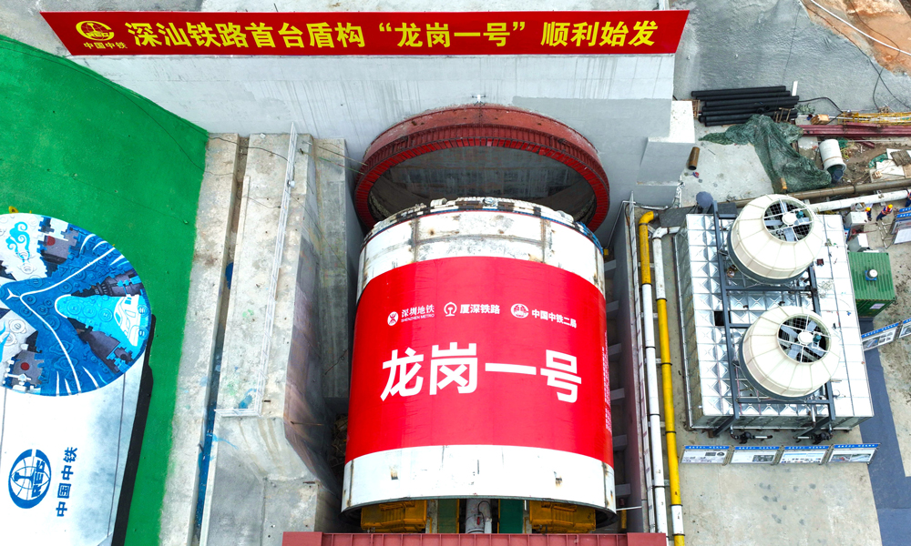深汕铁路是“八纵八横”高铁主通道中沿海高速通道的重要组成部分，起于深圳枢纽西丽站，终至深汕合作区并引入广汕铁路深汕站，正线全长125.52公里。由中铁二局组织施工的深汕铁路龙岗隧道盾构掘进全段并行厦深高铁，先后穿越21处重要建构筑物，长距离穿越岩溶及软硬不均与软硬交互不良地质，是深汕铁路重点控制性工程之一。龙岗隧道进口段分为南约和宝荷隧道两个区间，“龙岗一号”盾构机负责南约盾构区间的掘进任务。图为“龙岗一号”盾构机始发现场。