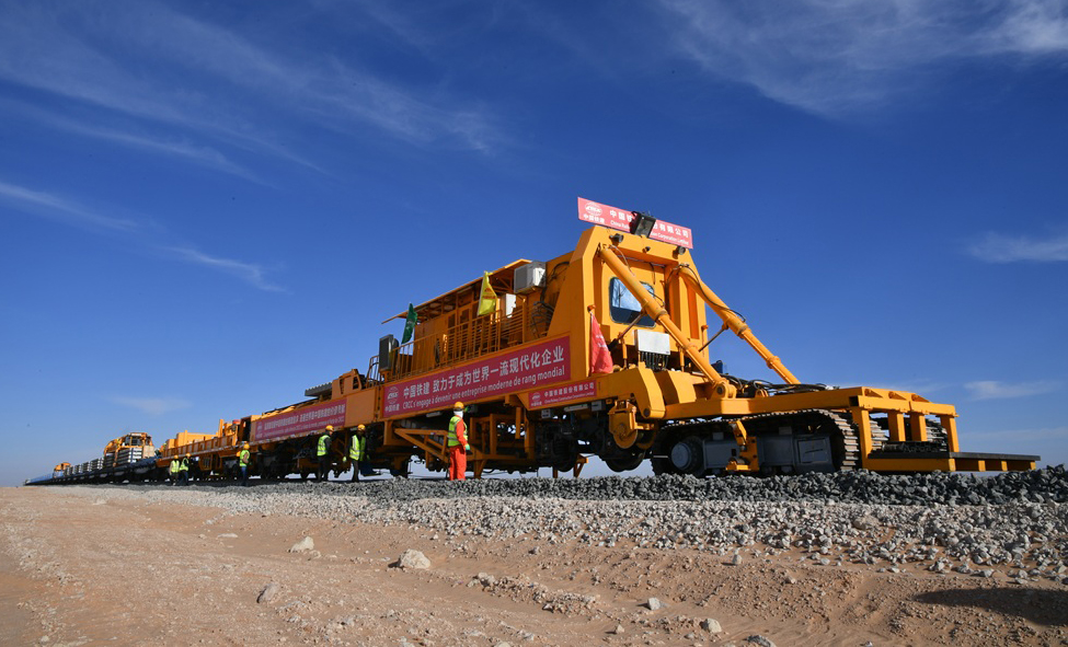 阿尔及利亚西部铁路矿业线项目全长950公里，中国铁建与当地国有企业承建了其中575公里，是中企在阿最大的基建工程，连接该国贝沙尔省和廷杜夫省加拉杰比莱特铁矿区。图为项目铺轨作业现场。